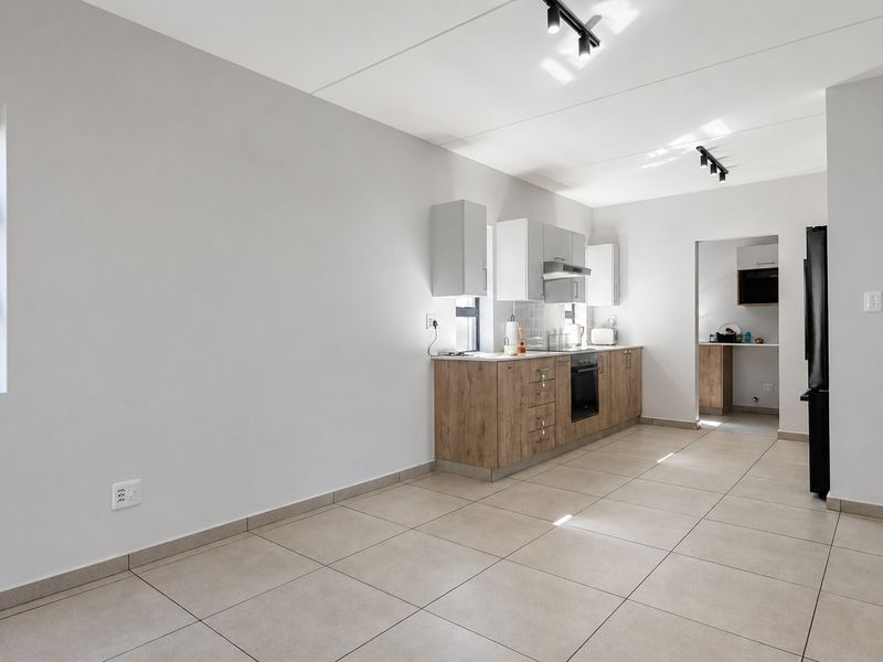 Modern open-plan kitchen featuring wood-finish cabinetry, built-in oven, extractor fan, and neutral tiled flooring, with an adjacent scullery area.