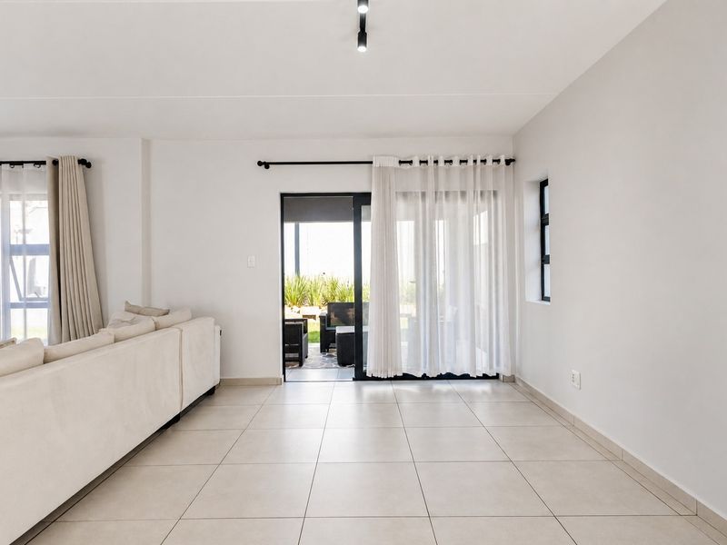 Bright and spacious living area featuring neutral tiled flooring, modern track lighting, and a sliding glass door providing access to the outdoor patio.