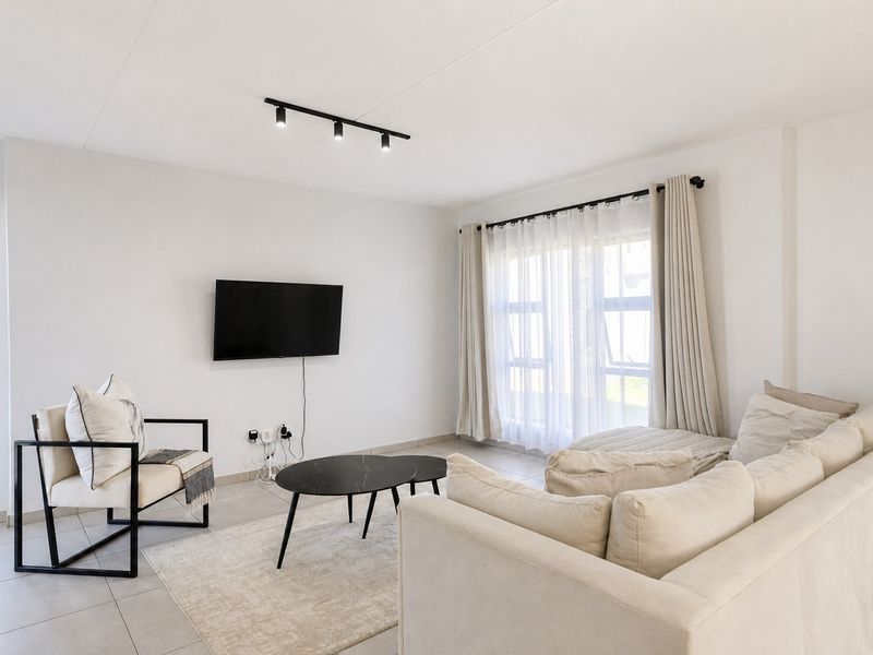 A bright and modern living room featuring neutral tiled flooring, contemporary track lighting, and large windows that provide ample natural light.