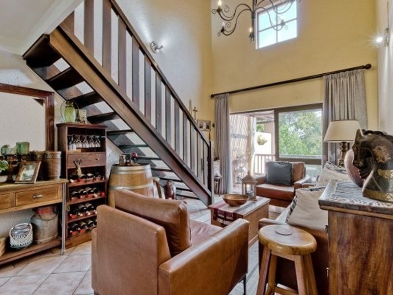 Spacious living room featuring a double-volume ceiling, a prominent wooden staircase with balustrade, tiled flooring, and large sliding doors leading to an outdoor area.