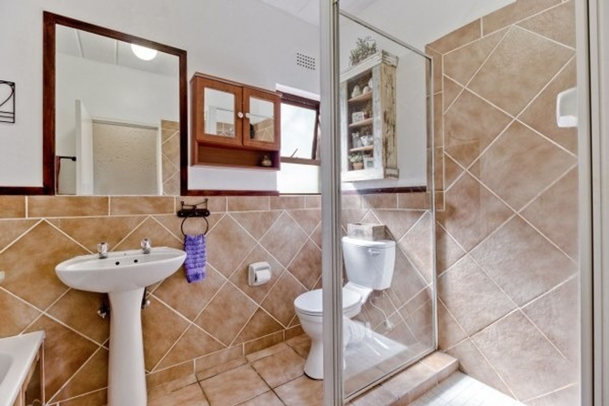 A functional bathroom featuring a pedestal basin, a glass-enclosed shower, and tiled finishes throughout.