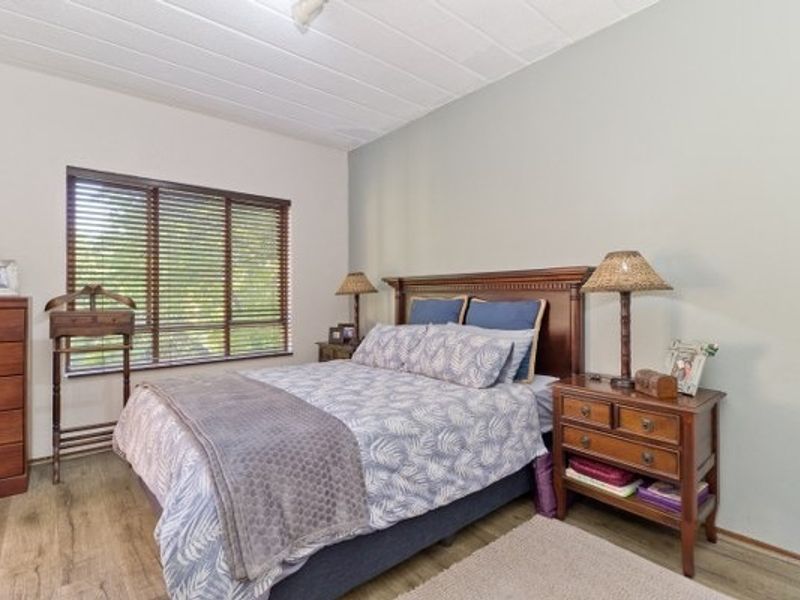 A well-lit bedroom featuring laminate flooring, a panelled ceiling, and large windows fitted with venetian blinds.
