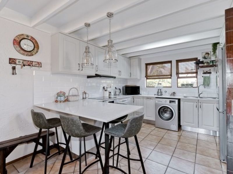A well-maintained kitchen featuring white shaker cabinetry, quartz countertops, subway tile backsplash, and exposed beam ceilings with integrated laundry facilities.