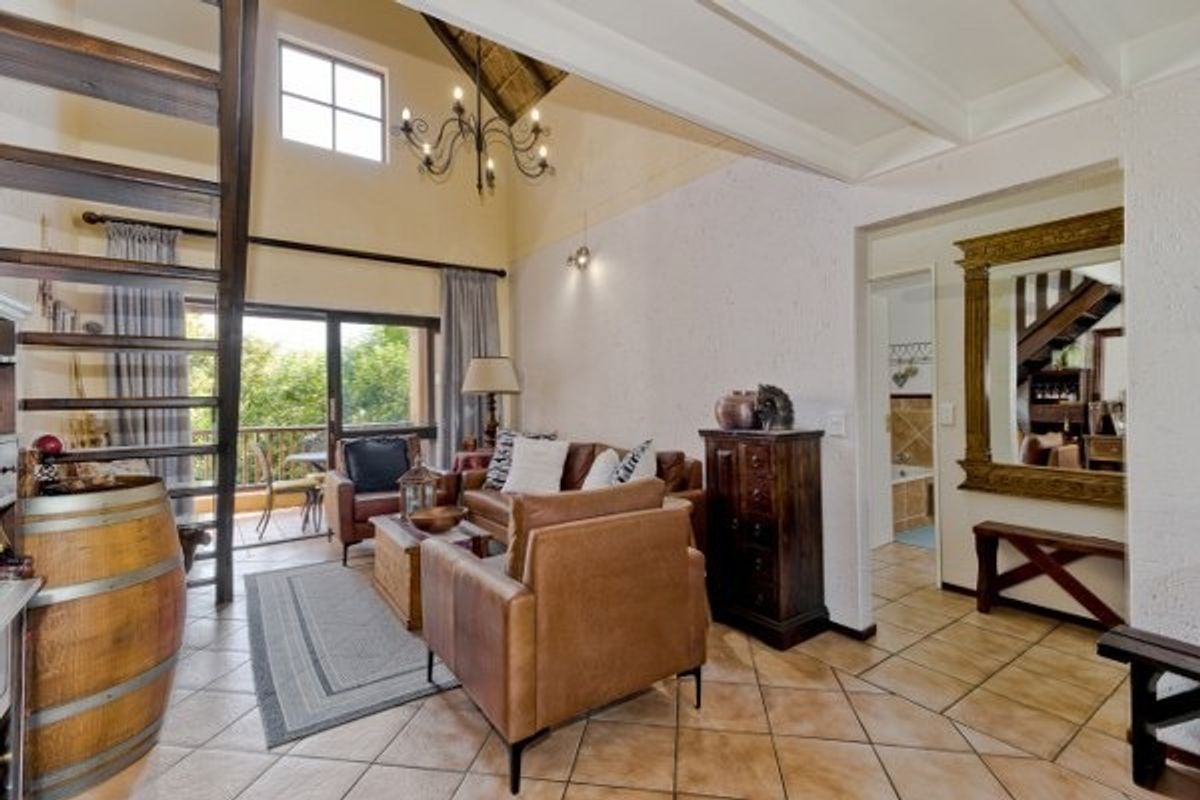 Spacious living room featuring high vaulted ceilings with exposed rafters, tiled flooring, and direct access to a private balcony through sliding glass doors.