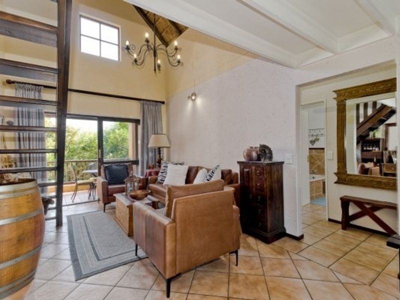 Spacious living room featuring high vaulted ceilings with exposed rafters, tiled flooring, and direct access to a private balcony through sliding glass doors.