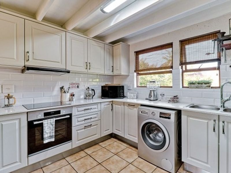A well-maintained kitchen featuring white cabinetry, subway tile backsplash, exposed ceiling beams, integrated appliances, and tiled flooring.