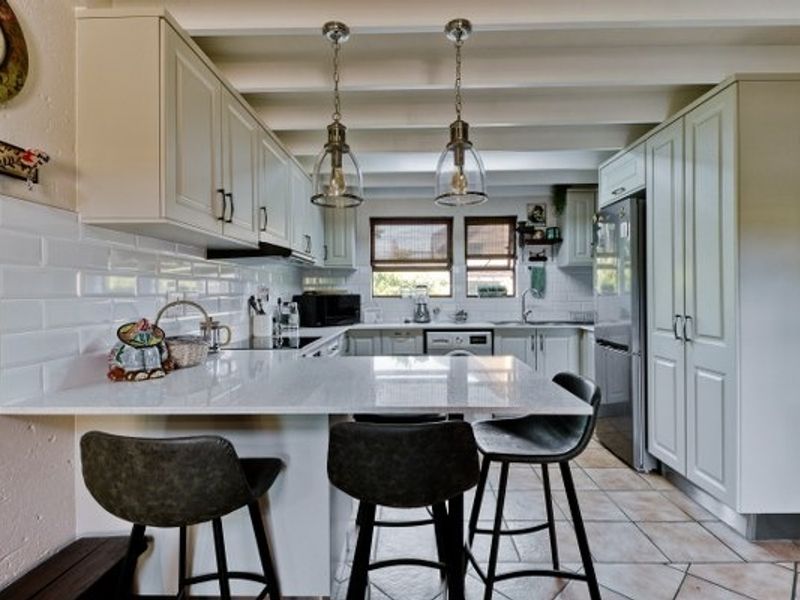 A well-appointed kitchen featuring white cabinetry, quartz countertops, subway tile backsplash, and exposed ceiling beams, creating a bright and functional culinary space.