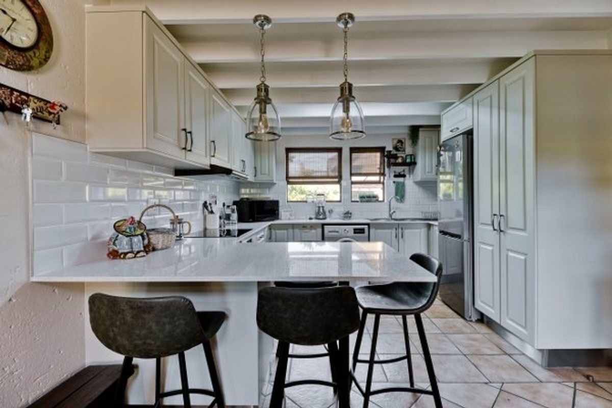 A well-appointed kitchen featuring white cabinetry, quartz countertops, subway tile backsplash, and exposed ceiling beams, creating a bright and functional culinary space.