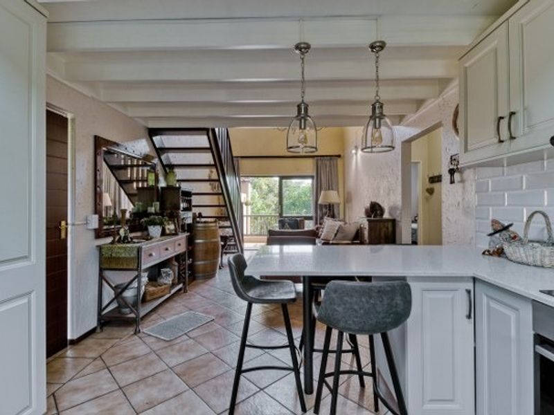 Open-plan kitchen and living area featuring white cabinetry, stone countertops, subway tile backsplash, exposed ceiling beams, and a staircase leading to the upper level.