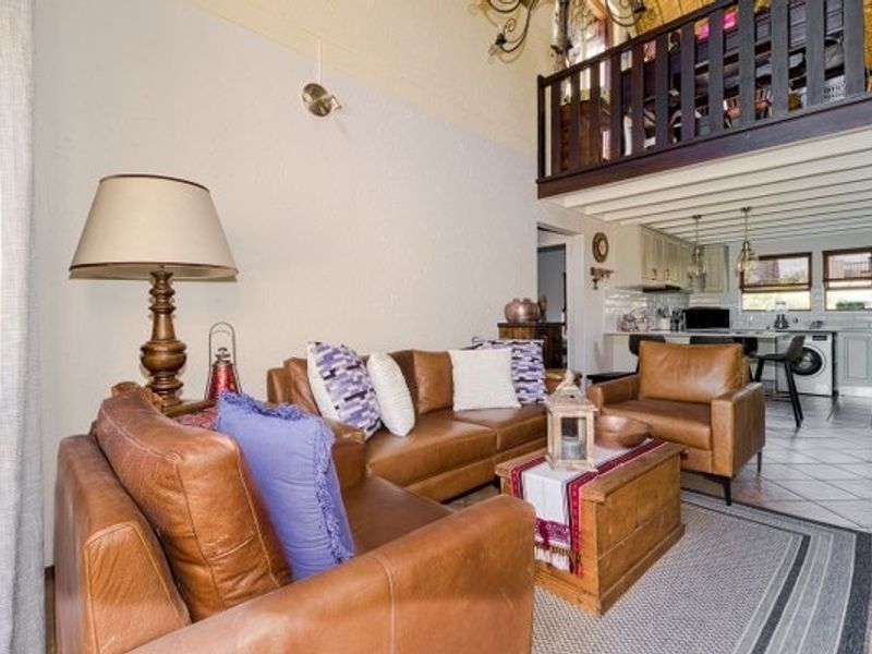 Open plan living area featuring a mezzanine level with wooden balustrade, exposed ceiling beams, and an adjoining kitchen with island and tiled flooring.