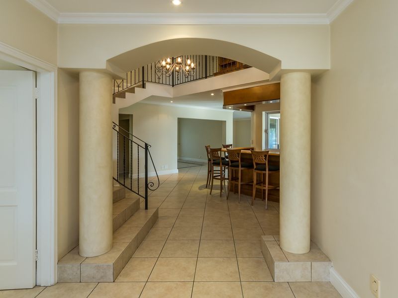Spacious living area featuring a grand arched entryway with columns, a built-in bar, and a staircase with decorative wrought iron railings.