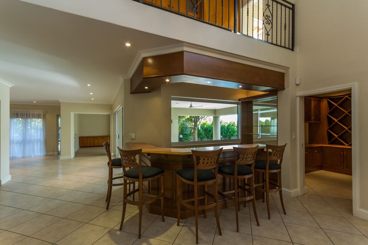 A spacious home bar area featuring a built-in wooden counter, recessed lighting, and a mezzanine level with a decorative wrought iron balustrade.