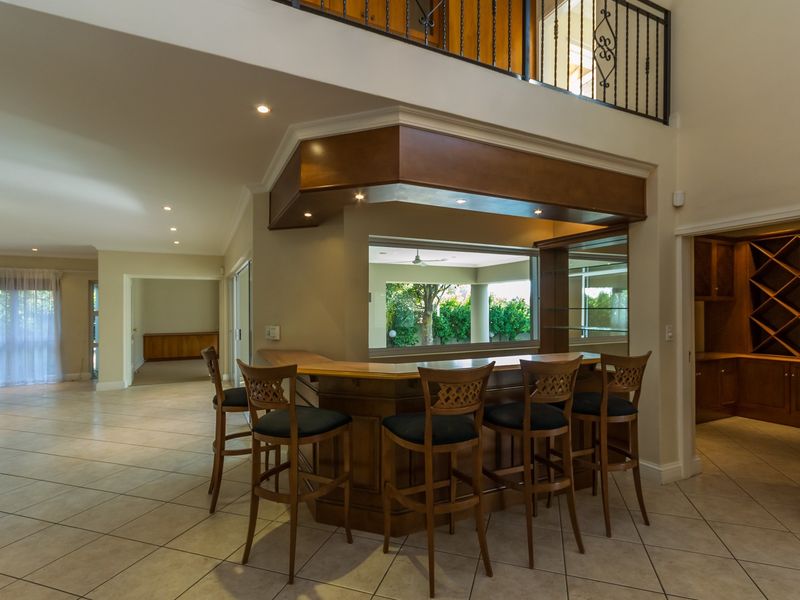 A spacious home bar area featuring a built-in wooden counter, recessed lighting, and a mezzanine level with a decorative wrought iron balustrade.