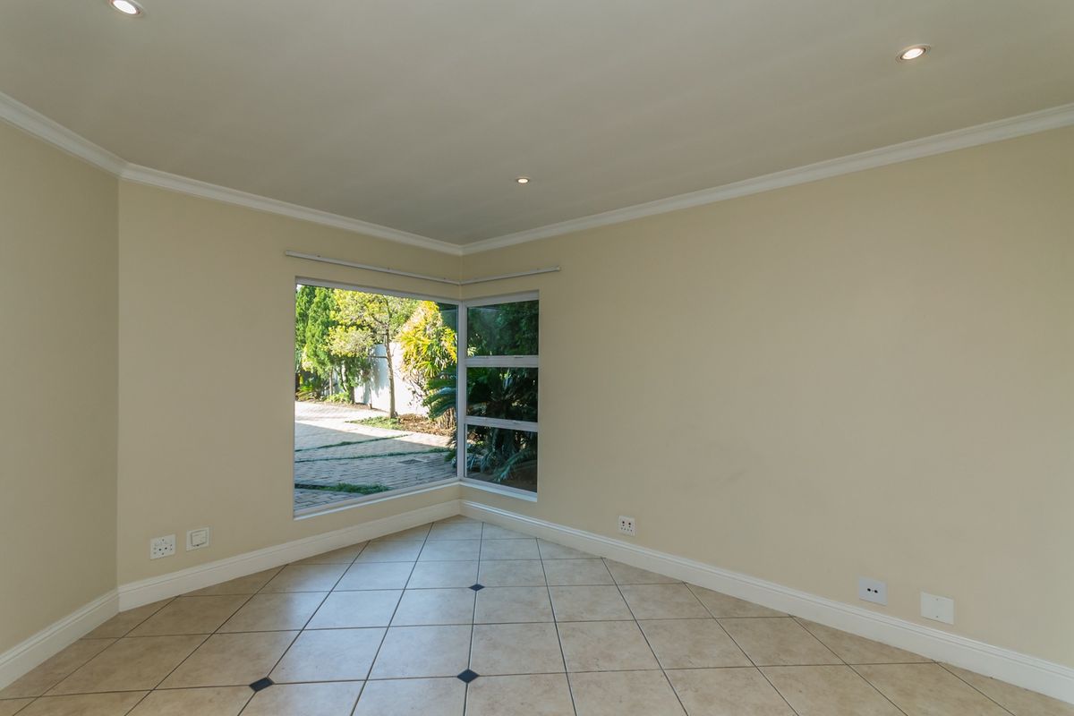 A bright, empty living area featuring neutral walls, tiled flooring, and a large corner window providing natural light and garden views.