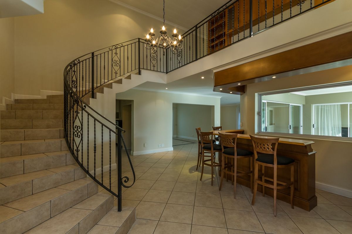 Spacious living area featuring a grand curved staircase with wrought iron railings, tiled flooring, and a built-in bar area.
