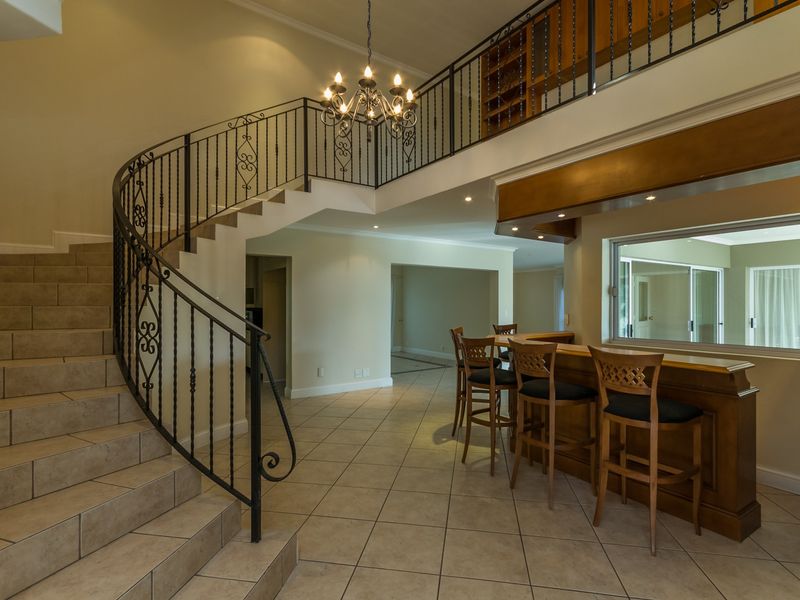 Spacious living area featuring a grand curved staircase with wrought iron railings, tiled flooring, and a built-in bar area.