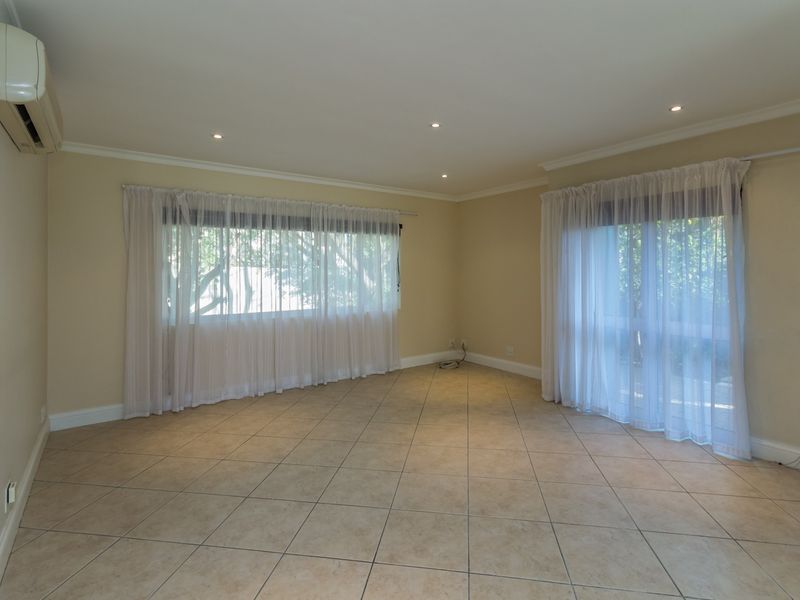 A spacious, empty living room featuring neutral tiled flooring, recessed downlighting, and a wall-mounted air conditioning unit with access to the outdoors.
