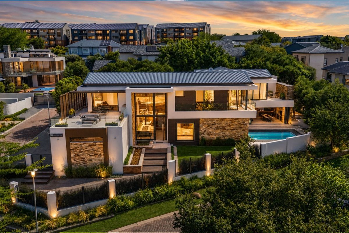 Stunning aerial view of a modern luxury residence featuring stone accents, expansive glass facades, a private swimming pool, and landscaped outdoor areas.
