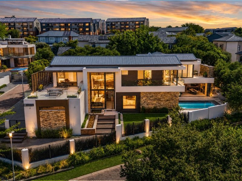 Stunning aerial view of a modern luxury residence featuring stone accents, expansive glass facades, a private swimming pool, and landscaped outdoor areas.