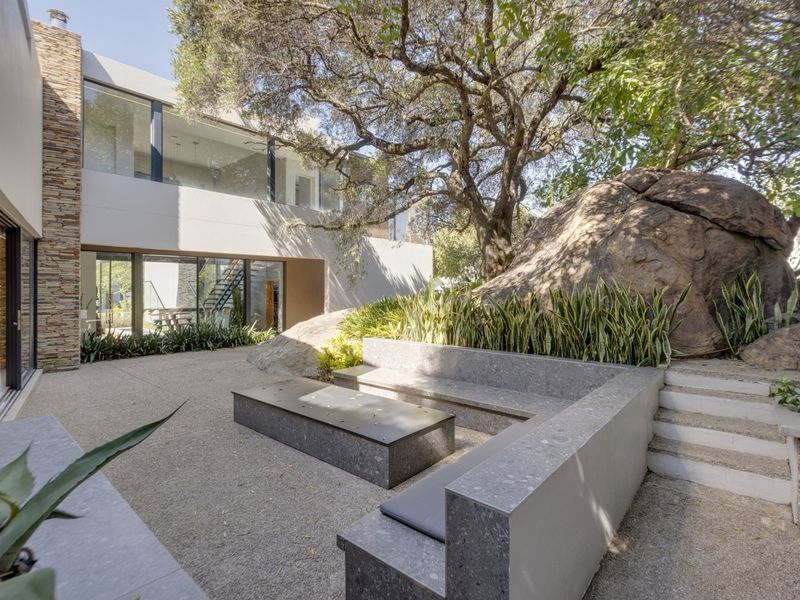 A modern outdoor patio area featuring built-in stone seating, a large natural boulder, and seamless access to the interior through sliding glass doors.