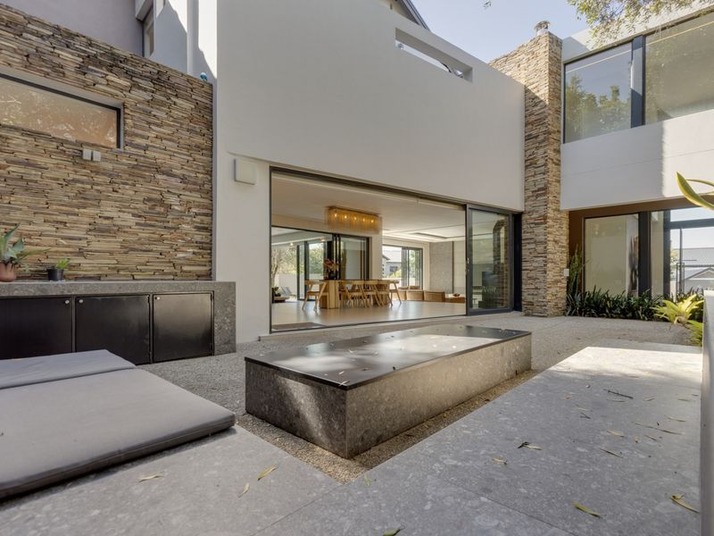 Modern outdoor patio featuring stone cladding, a built-in stone bench, a central water feature, and large sliding glass doors leading into the living area.
