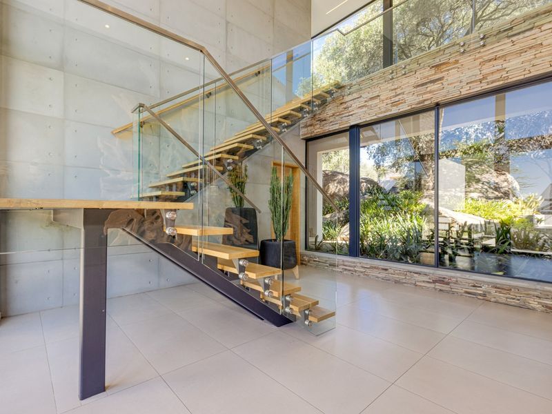 Modern entrance hall featuring a striking floating staircase with glass balustrades, concrete feature wall, and expansive windows overlooking the garden.