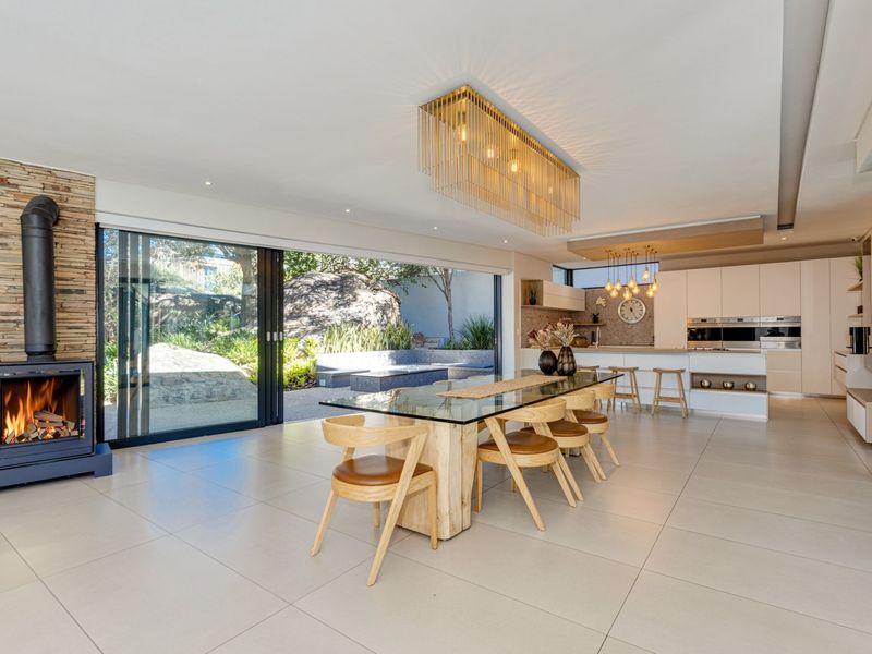 Spacious open-plan living and dining area featuring a stone-clad fireplace, modern kitchen with integrated appliances, and seamless flow to the outdoor patio.