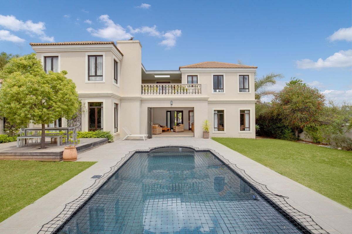 Rear view of a two-story residence featuring a swimming pool with safety net, timber decking, a tiled patio, and an upper-level balcony.
