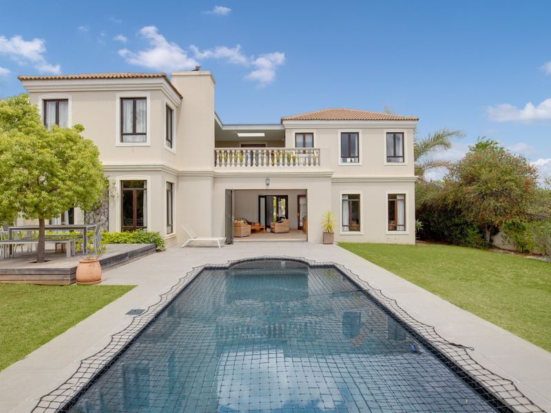 Rear view of a two-story residence featuring a swimming pool with safety net, timber decking, a tiled patio, and an upper-level balcony.