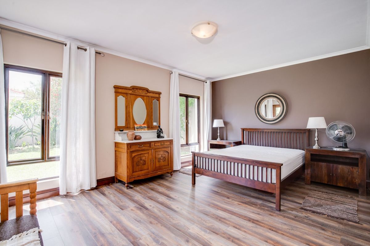 Spacious bedroom featuring modern laminate flooring, neutral wall tones, and large windows providing natural light and garden views.