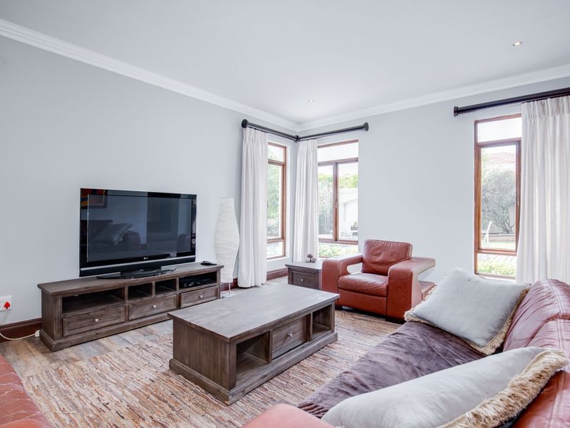 A bright and well-maintained living room featuring crown molding, recessed downlights, and large windows with timber frames overlooking the garden.