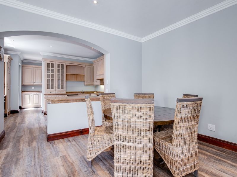 Open-plan dining area featuring laminate flooring and crown molding, flowing into a well-appointed kitchen with granite countertops and classic cabinetry.