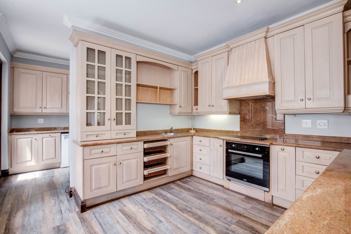 A well-maintained kitchen featuring light wood cabinetry, granite countertops, integrated oven, and extractor hood, complemented by modern wood-look laminate flooring.
