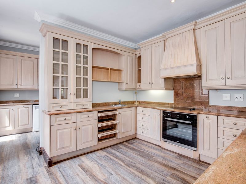 A well-maintained kitchen featuring light wood cabinetry, granite countertops, integrated oven, and extractor hood, complemented by modern wood-look laminate flooring.