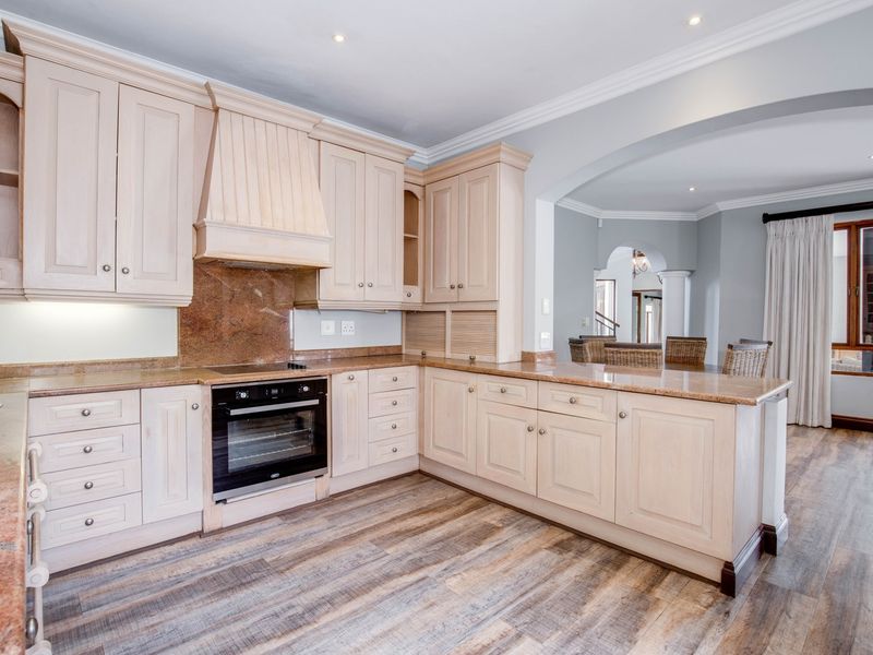 Spacious kitchen featuring light wood cabinetry, granite countertops, built-in oven, and hob, with an open-plan layout leading into the adjacent living area.