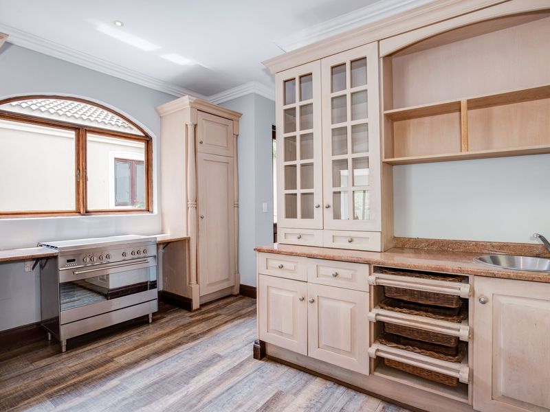 A bright, well-maintained kitchen featuring light wood cabinetry, granite countertops, a stainless steel oven, and an elegant arched window.