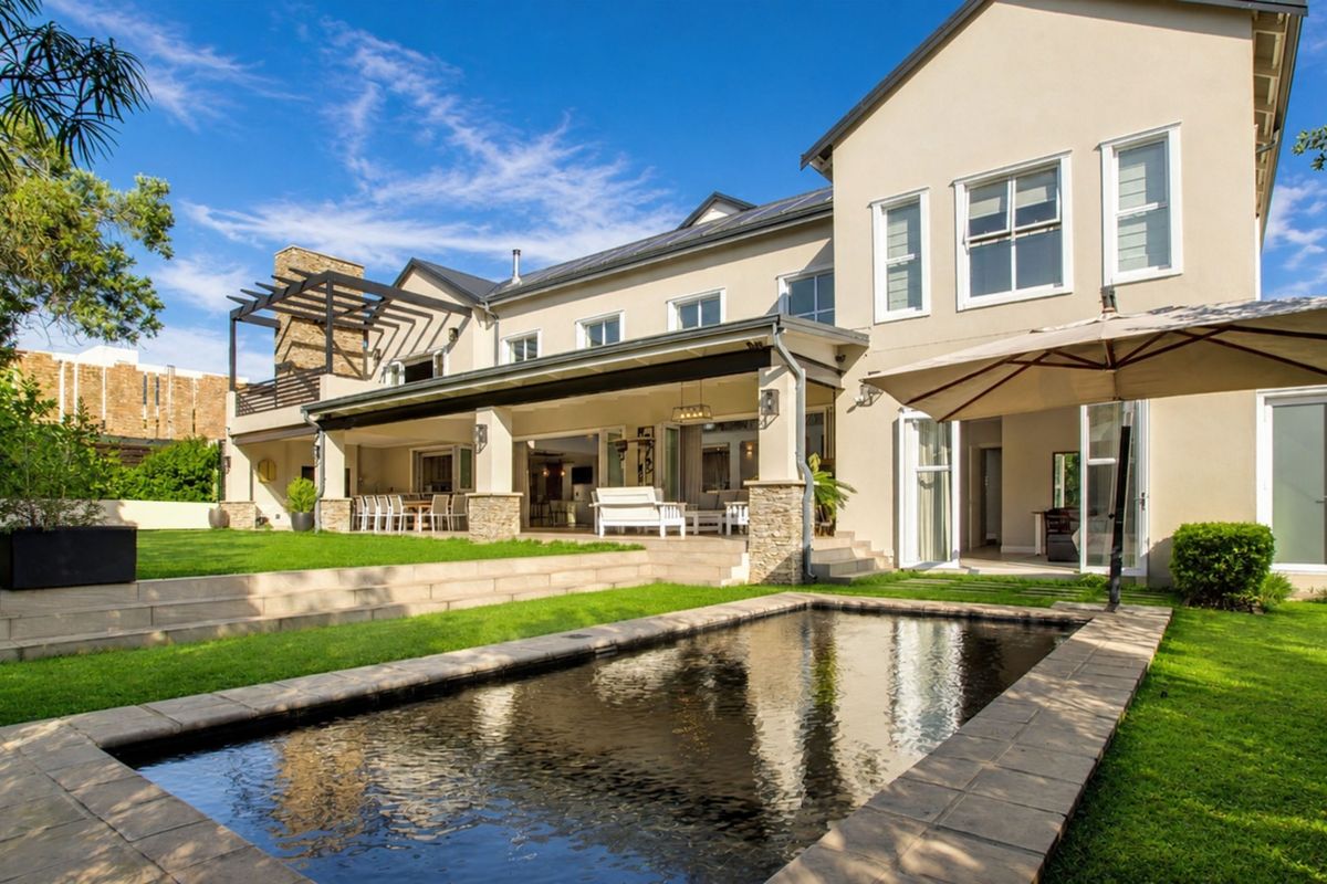 Spacious rear exterior featuring a swimming pool, expansive covered patio with stone detailing, and a well-maintained garden, perfect for outdoor entertaining.