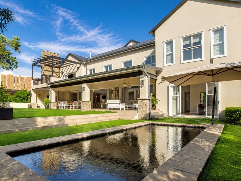 Spacious rear exterior featuring a swimming pool, expansive covered patio with stone detailing, and a well-maintained garden, perfect for outdoor entertaining.