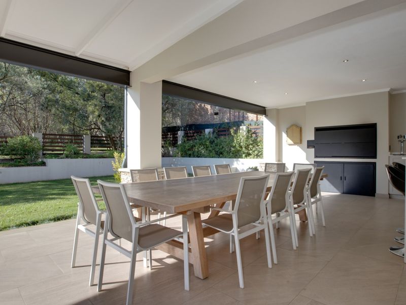 Spacious covered patio featuring a built-in braai, outdoor sink, and tiled flooring, seamlessly connecting to the garden area.