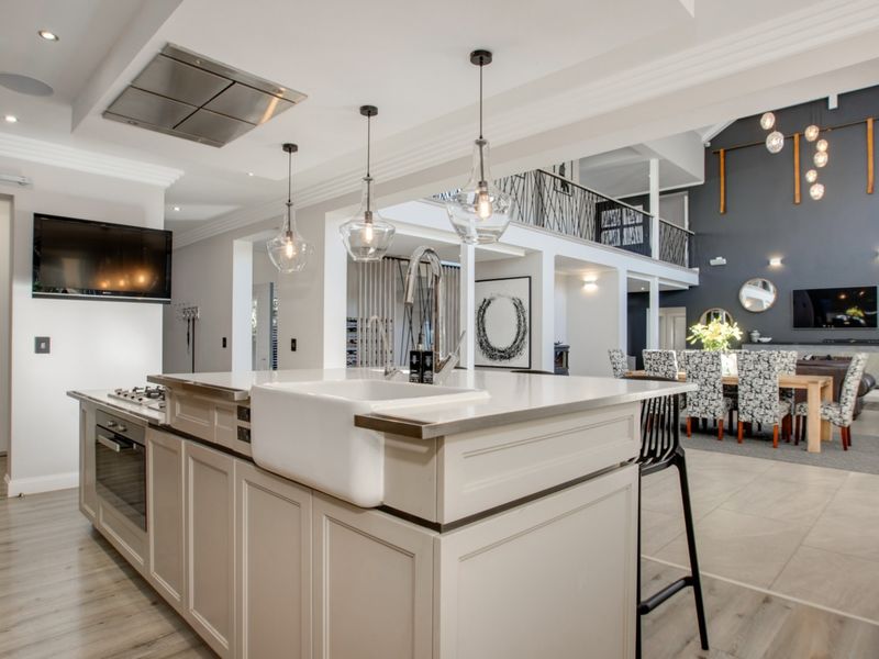 Spacious open-plan kitchen and living area featuring a large island with apron-front sink, modern built-in appliances, and a striking double-volume ceiling with mezzanine.