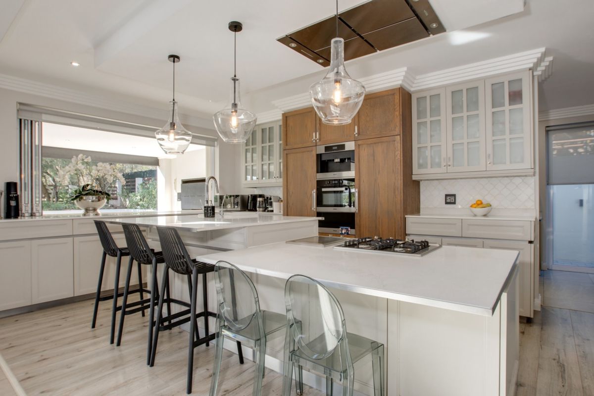Modern kitchen featuring a large island with quartz countertops, built-in appliances, glass-front cabinetry, and stylish pendant lighting, creating a bright and functional culinary space.