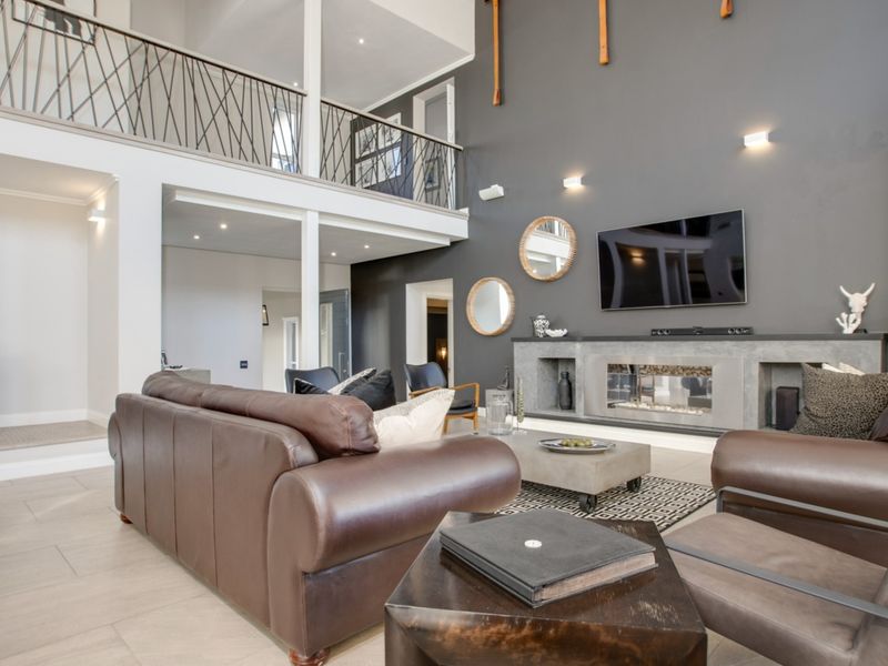 Spacious double-volume living room featuring a modern built-in fireplace, a freestanding wood-burning stove, and an open mezzanine level with decorative iron railings.