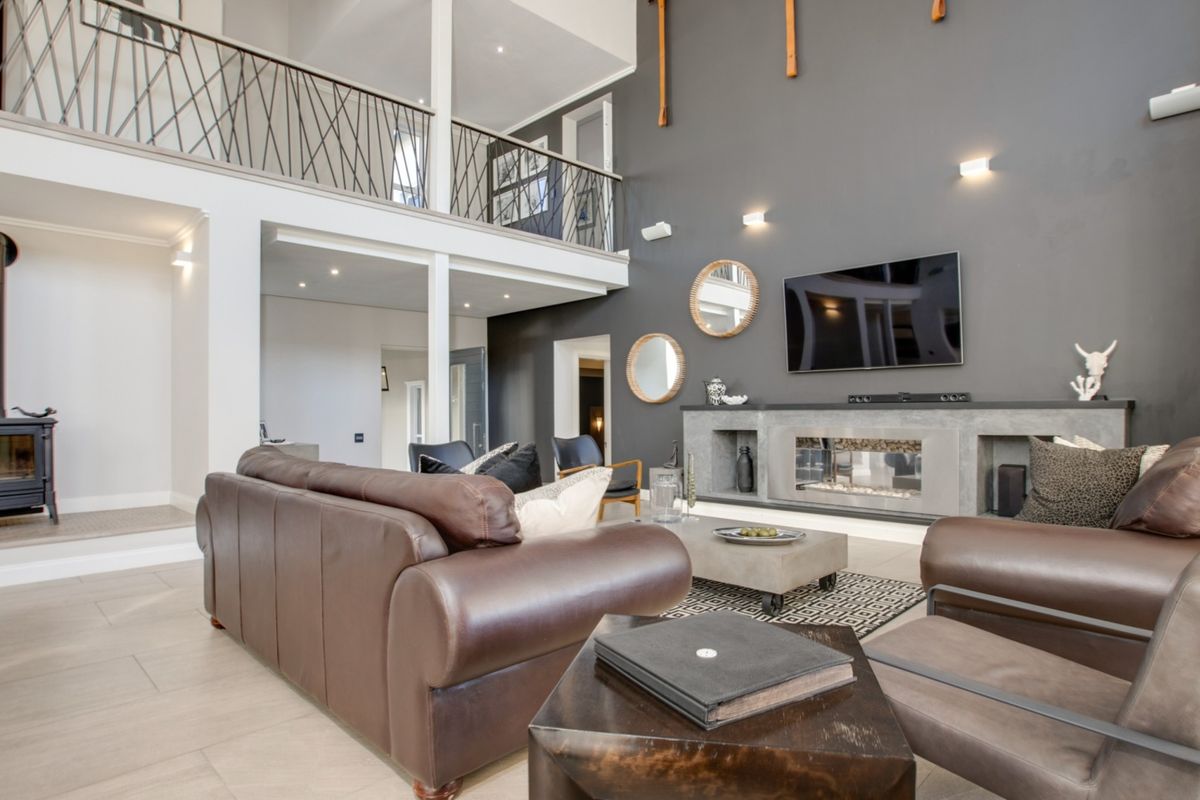 Spacious double-volume living room featuring a modern built-in fireplace, a freestanding wood-burning stove, and an open mezzanine level with decorative iron railings.