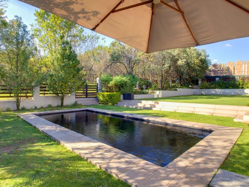 A well-maintained outdoor pool area featuring stone coping, tiered retaining walls, and a landscaped garden with timber fencing.