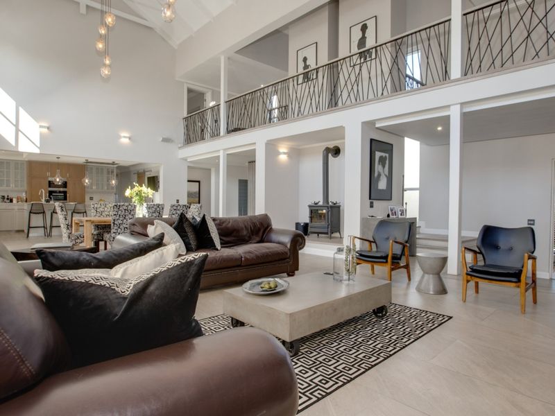 Spacious open-plan living area featuring a double-volume vaulted ceiling, mezzanine level with decorative balustrade, tiled flooring, and a modern freestanding fireplace.