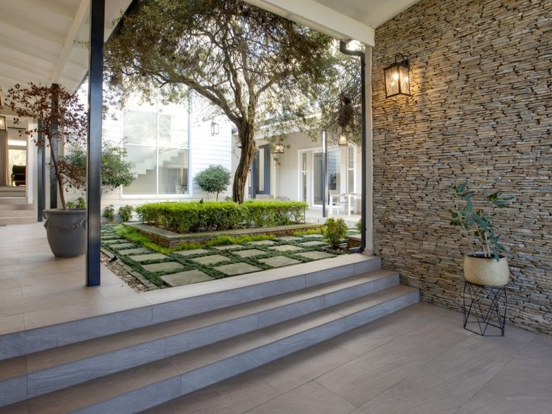 A beautifully designed covered patio featuring a striking stone-clad feature wall, modern tiled flooring, and seamless access to a landscaped courtyard garden.