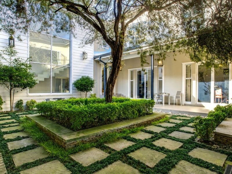 A beautifully landscaped rear courtyard featuring a central raised garden bed, paved pathways, and a covered patio area with large glass doors.