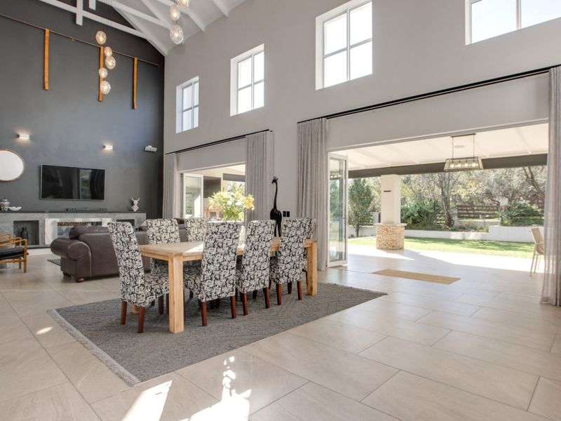 Spacious open-plan living and dining area featuring high vaulted ceilings, exposed rafters, large sliding doors to the patio, and a modern built-in fireplace.