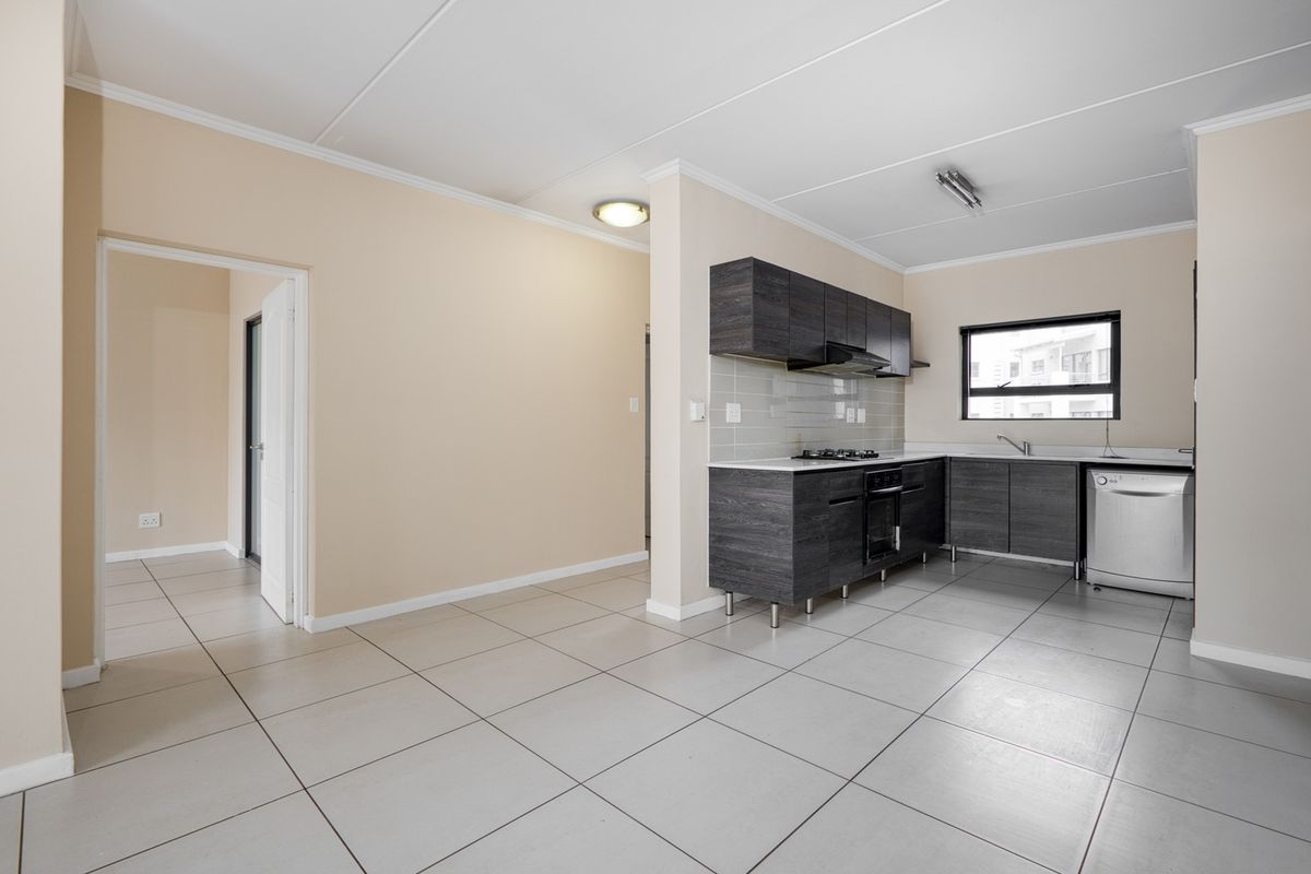 A clean, modern kitchen featuring dark wood-look cabinetry, a gas hob, built-in oven, and neutral tiled flooring in an open-plan layout.