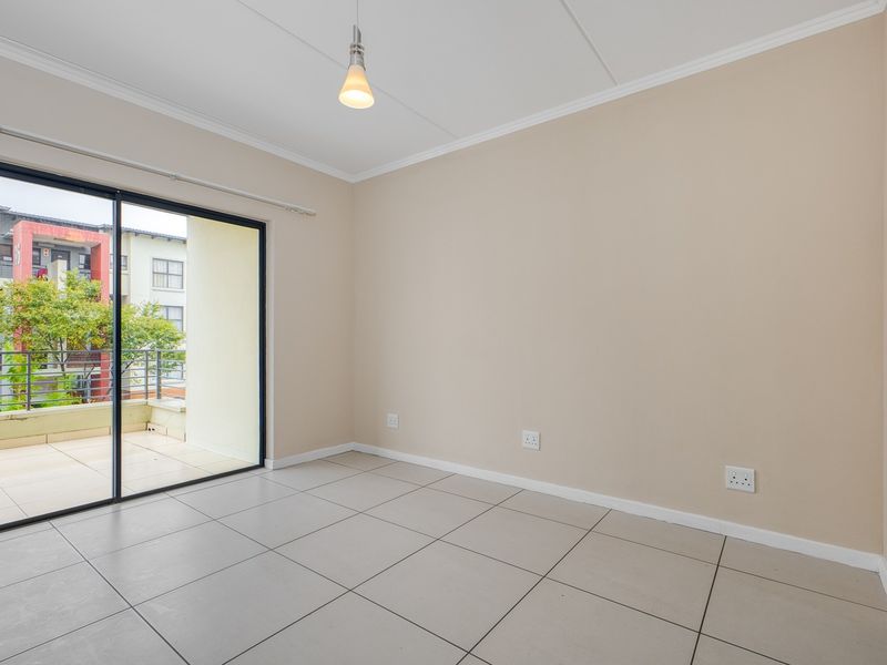 A bright, empty living room featuring neutral tiled flooring, coved ceilings, and a large sliding glass door providing access to an outdoor balcony.